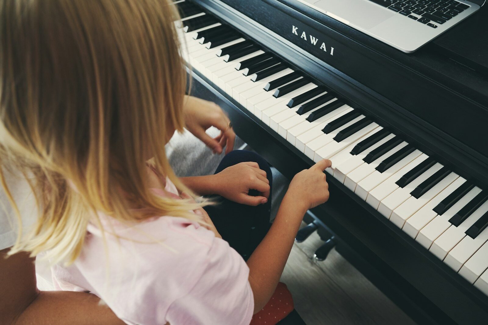 Young girl plays piano with laptop nearby